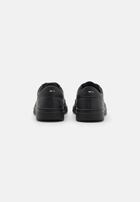 Schwarze Ledersneaker mit glatter Oberfläche, flachen Gummisohlen und minimalistischer Gestaltung. Mit kleinen Farbakzenten an der Ferse.