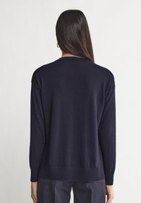 Mörkblå stickad tröja med långa ärmar, ribbade muddar och kant. Mjuk textur med en avslappnad passform och rund halsringning.