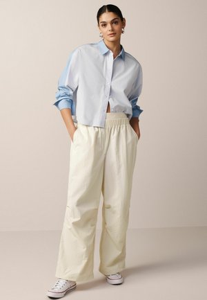 Hvid og lyseblå cropped button-up skjorte med lange ærmer, parret med løstsiddende, cremede elastiske bukser og hvide sneakers.