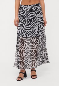 Maxi skirt in sheer fabric featuring a black and white leaf pattern. Elastic waistband, flowy design, and side slit for movement.