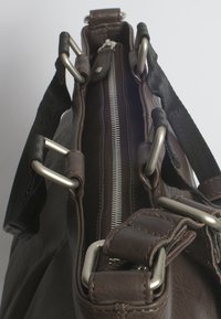 Bruine leren tas met een zilveren rits, brede opening en metallic hardware. Beschikt over stoffen strapaccenten en robuuste constructie.