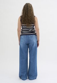 Randig ärmlös topp i marinblått och krämfärgat, i kombination med vida denimjeans. Jeansen har en ljusblå tvätt och inga synliga detaljer.