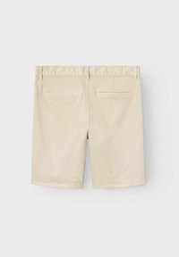 Lys beige bomuldsshorts med lige snit, der har to baglommer og bæltestropper. Glat tekstur med minimale syninger.