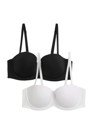 Mujer con sujetador blanco acolchado y ropa interior de talle alto a juego, posando con un brazo levantado y mirando hacia abajo.