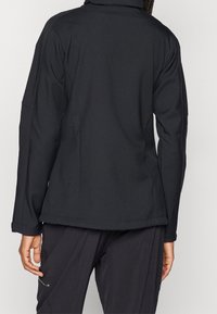 Czarna kurtka z miękkiej tkaniny soft-shell, z wysokim kołnierzem, długimi rękawami i dopasowanym krojem. Gładka faktura z subtelnymi szwami, bez widocznych elementów metalowych.