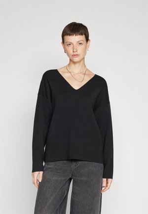 Black V-neck sweater with long sleeves, relaxed fit, made of soft fabric, paired with gray high-waisted jeans. Minimalistic design, no patterns.