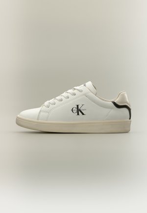 Baskets basses blanches Calvin Klein avec semelle beige, devant lacé et logo noir sur le côté sur fond neutre.