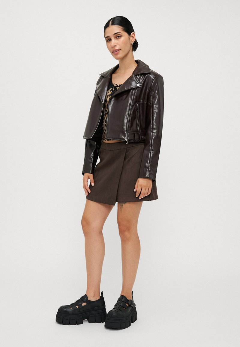 Veste courte en simili cuir marron, top à imprimé léopard, mini jupe marron et chaussures à plateforme noires épaisses avec découpes et semelles massives.