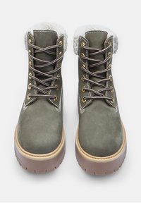 Stivali verde oliva con lacci realizzati in camoscio, con un colletto in pelliccia sintetica, suola in gomma beige e occhielli dorati per i lacci.