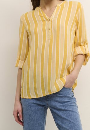 Camicia gialla a righe con colletto a notched, chiusura con bottoni e maniche arrotolate, realizzata in tessuto leggero, abbinata a jeans blu.