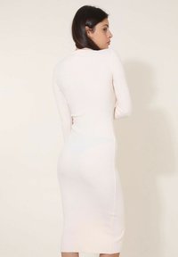 Robe midi côtelée en doux tissu blanc, avec des manches longues et une silhouette ajustée. La vue de dos montre des fentes latérales subtiles.