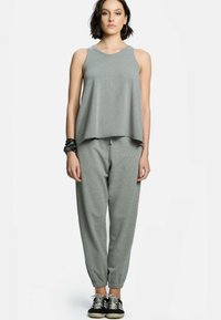 Szara koszulka bez rękawów o luźnym kroju, zestawiona z szarymi spodniami dresowymi z elastycznymi mankietami. Model nosi czarno-białe sneakersy.