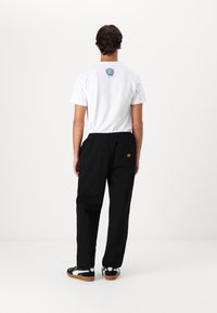 Hvid T-shirt med grafisk print på ryggen, parret med sorte bukser med elastisk talje og sorte sneakers med hvide detaljer.