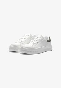Hvite sneakers laget av glatt lær med en teksturert grå aksent på hælen, med tykk, riptet såle og tradisjonelle lisser.