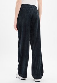 Szerokie kordowe spodnie w ciemnym granacie, z teksturowaną prążkowaną powierzchnią, elastycznym pasem i luźnym krojem, zestawione z białymi trampkami.