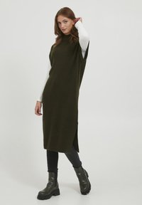 Abito a coste verde oliva con colletto alto, fessure laterali e maniche corte, abbinato a leggings neri e stivali neri chunky.