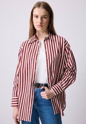Rood-wit gestreepte button-up shirt met een kraag, borstzak en lange mouwen, gecombineerd met hoogsluitende blauwe spijkerbroek en een zwarte riem.