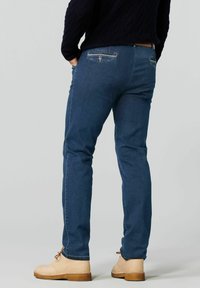 Jeans en denim bleu foncé avec une coupe slim, présentant un design de poche arrière et un tissu légèrement texturé, associés à des bottines beiges à la cheville.