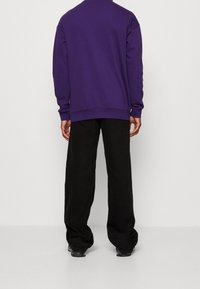 Felpa viola con un taglio loose, caratterizzata da maniche lunghe e polsini a coste, abbinata a pantaloni neri a gamba larga. Texture liscia.