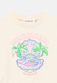 Φούτερ στο χρώμα της κρέμας με λαμπερό σχέδιο κοχυλιού με φοινικόδεντρα, ζωντανά μπλε και πράσινα χρώματα, και το κείμενο «ΑΝΟΙΞΕ ΤΗΝ ΚΑΡΔΙΑ ΣΟΥ».