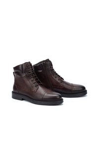 Botas de tobillo de cuero marrón con punta redondeada, cierre con cordones, cremallera lateral y suela de goma texturizada. Presenta detalles de costura.
