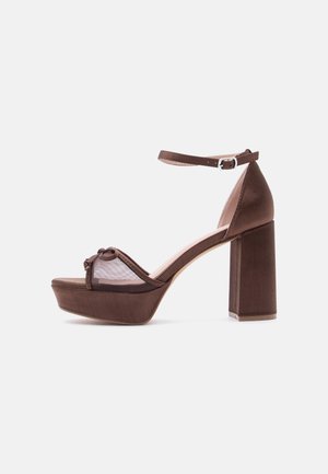 Sandales à plateforme marron avec un large talon bloc, finition satinée, bout ouvert et panneau en maille. Elles présentent une fine bride de cheville avec une boucle et un accent nœud.