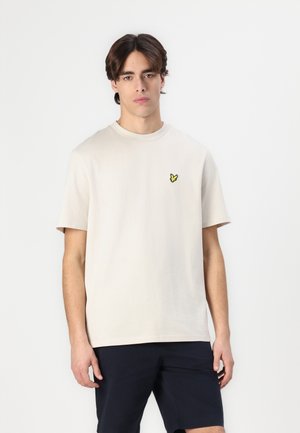 T-shirt en coton beige avec un col rond, des manches courtes et un logo de papillon jaune sur la poitrine gauche. Design simple et décontracté.