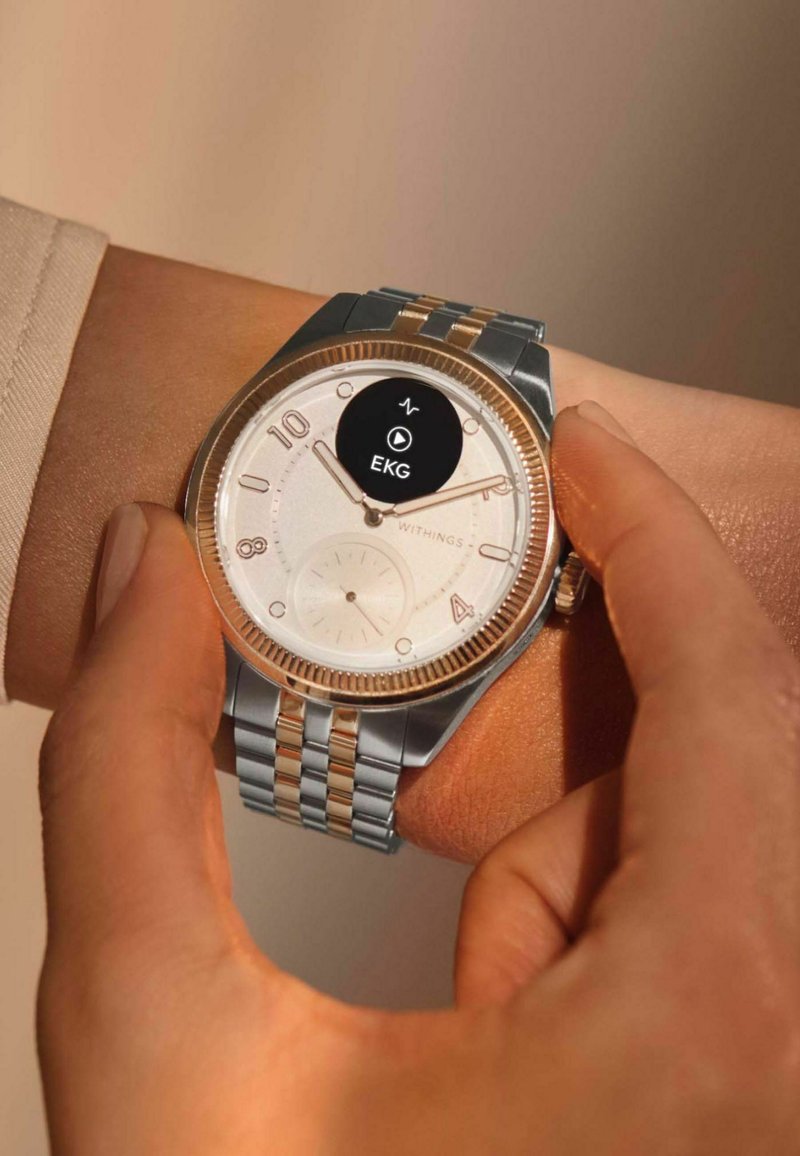 Silberne und goldfarbene Smartwatch mit einem runden weißen Ziffernblatt, großen Zahlen und einer auf dem Bildschirm angezeigten EKG-Funktion. Metallarmband mit Gliedern.