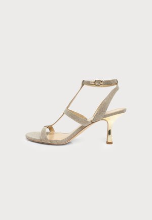 Sandale beige à brides avec un talon haut fin doré brillant et une boucle en or, vue de côté sur un fond uni.