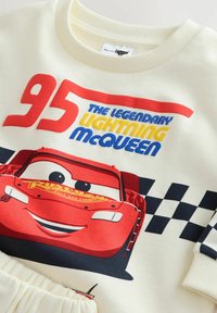 Sudadera blanca con un gráfico de Lightning McQueen en rojo, con el número "95" y texto en azul y amarillo, acentuado por un patrón de tablero de ajedrez negro.