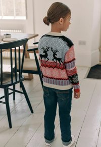 Maglione lavorato a maglia con motivi colorati, che presenta renne e fiocchi di neve in blu, rosso e nero, abbinato a jeans in denim blu.