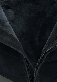 Wnętrze czarnych zamszowych butów, charakteryzujące się gładką fakturą, pionowym zamkiem błyskawicznym oraz kanciastym kształtem bez widocznych wzorów.