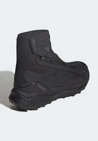 Baskets montantes noires de sport avec une couche Gore-Tex, un tissu texturé, une fermeture éclair sur le côté et une semelle extérieure robuste avec un relief prononcé.