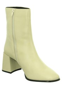 Bottine beige à bout pointu, en cuir lisse, avec une fermeture éclair latérale et un talon carré épais. Détail de semelle extérieure noire à la base.