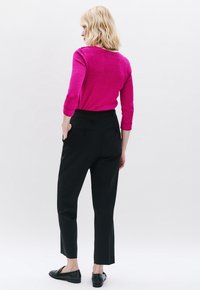 Figurbetontes, strukturiertes, rosafarbenes Sweatshirt mit Dreiviertelärmeln, kombiniert mit schicken schwarzen Hosen und schwarzen Loafers. Modell von hinten gezeigt.