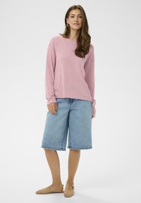 Haut rose pâle à manches longues associé à des culottes larges en denim bleu et des ballerines tissées beiges, avec une coupe décontractée et une texture douce.