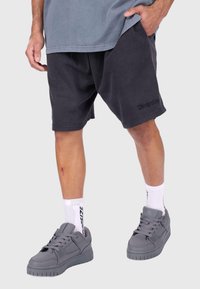 Dunkelgraue, strukturierte Shorts mit elastischem Bund und kleinem Logo, kombiniert mit grauen Sneakern und weißen Socken mit schwarzen Akzenten.