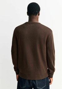 Brązowy sweter z dzianiny z prążkowanym dołem i mankietami. Projekt ma okrągły dekolt i fakturowaną powierzchnię.