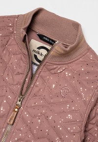 Gequilted roze jas met gouden spikkels, geribbelde kraag en rits aan de voorkant. Kenmerkt zich door een ronde logo en textiel met textuur.