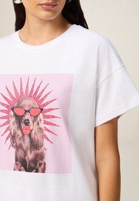 Witte katoenen T-shirt met een grote roze grafiek van een hond in een zonnebril, versierd met roze strass-steentjes en zonnestraalontwerpdetails.