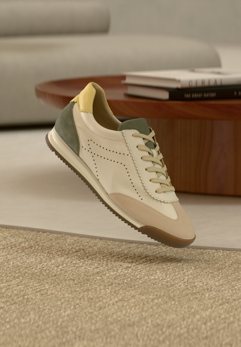 Baskets beige clair avec des accents verts et jaunes, en cuir lisse, design perforé, et une semelle en caoutchouc, présentées au-dessus d'un tapis texturé.