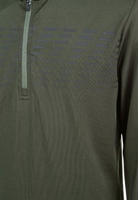 Grøn pullover skjorte med en kvart lynlås, der har et struktureret mønster af mørke striber over den øverste front. Glat stof, lange ærmer.
