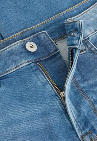Blue denim jeans with an unzipped brass zipper and a secured metal button on the waistband with orange stitching details.