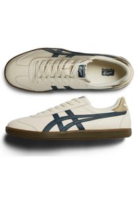 Krémové kožené tenisky s námořnickými pruhy, gumičkovou podrážkou, kulatou špičkou a šněrováním. Branding na jazyku. Klasický design.