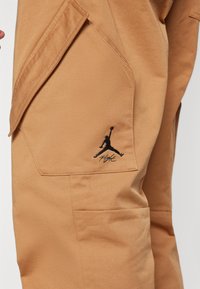Bež cargo hlače z velikim stranskim žepom in vezenim črnim logotipom Jordan s podnapisom "Flight".