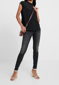 Sort ærmeløs top med høj hals, kombineret med mørke skinny jeans og nude sandaler med blokhæl. Lille håndtaske med kæderem.