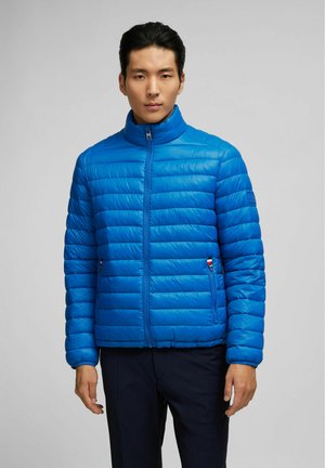 Blauwe gewatteerde pufferjack met een hoge kraag, vooraan met ritssluiting, verticale naden en twee ritszakken aan de zijkant, met een klein logoaccent.
