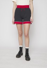 Shorts deportivos negros con una cintura elástica roja y acentos rojos en el dobladillo. Incluye detalles de pipings blancos y cordón ajustable.