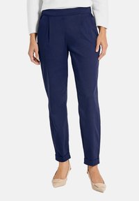 Marineblauwe op maat gemaakte broek van een gladde stof, met voorplooien en opgerolde zoom, gecombineerd met lichtbeige flats.