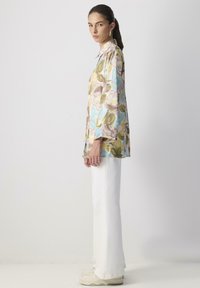 Long-sleeve blouse in pastel colors with floral patterns, made of lightweight fabric. Paired with white wide-leg pants and beige sneakers.